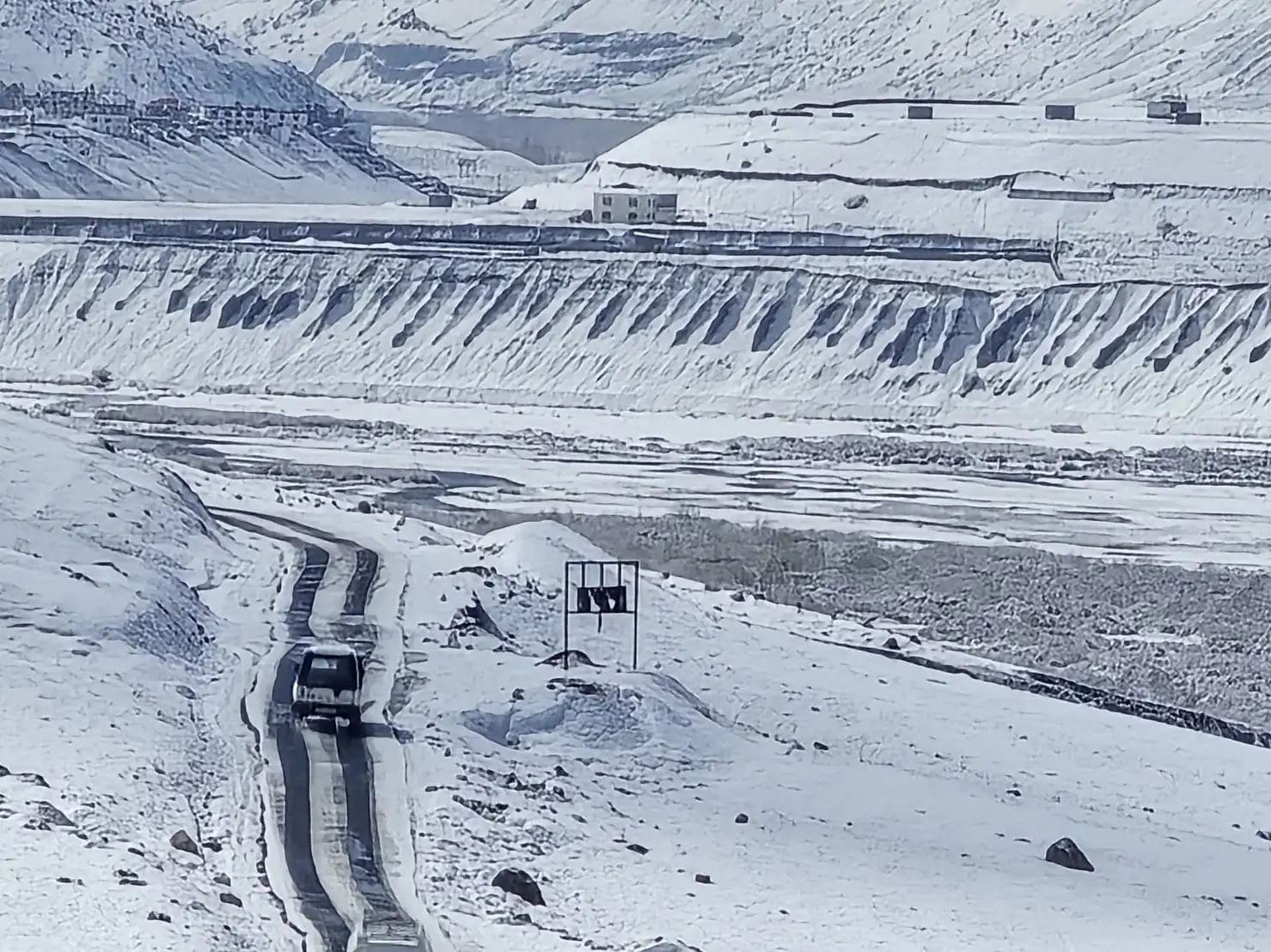 A car on a narrow road cleared through snow in the Spiti valley, with white slopes all around