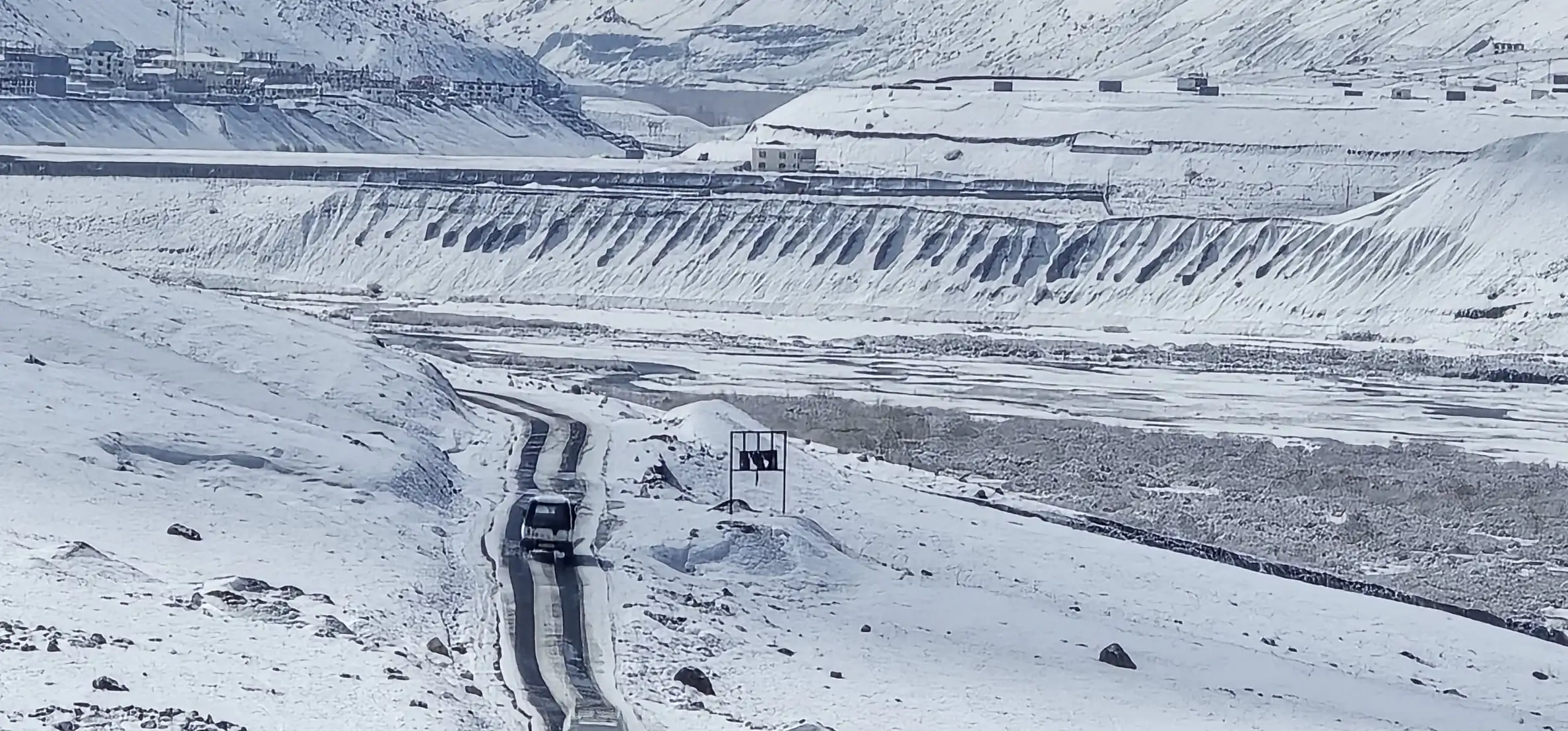 A car on a narrow road cleared through snow in the Spiti valley, with white slopes all around
