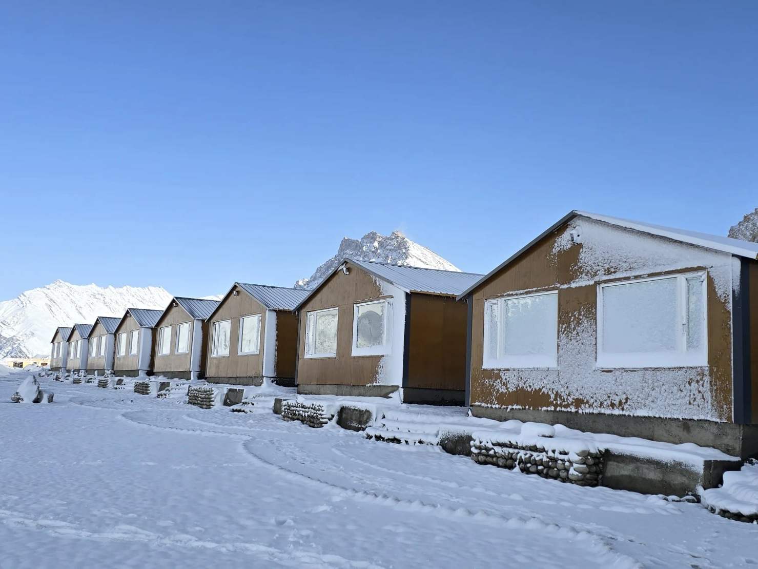 Spiti Villa’s cottages under fresh snow, with Key Monastery on the ridge behind