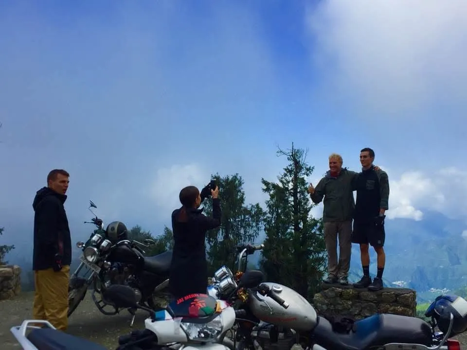 Riders take photos at a misty roadside viewpoint, with their motorcycles parked in front