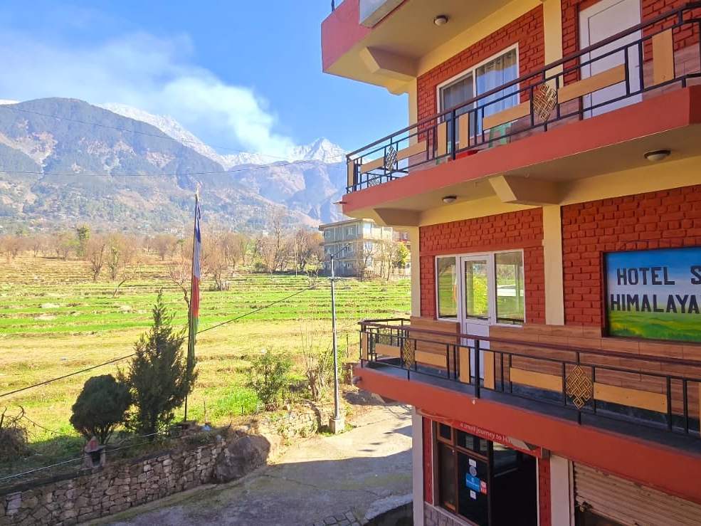 Hotel Samdupling’s red-brick front and balconies, with green fields and the Dhauladhar behind