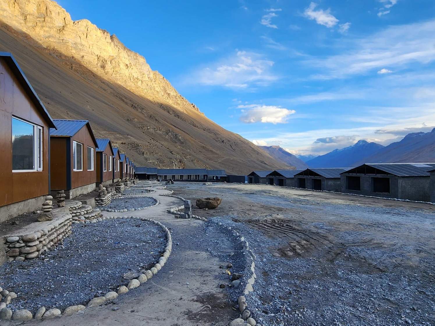 Spiti Villa’s wooden cottages in summer, along a gravel path below bare mountains